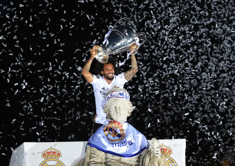 Marcelo wearing a Real Madrid shirt lifts the Champions League trophy next to a statue